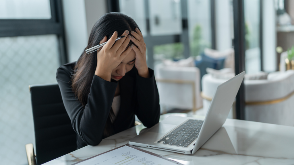 Young woman sitting at a desk with a laptop, holding her head in frustration, representing the risks foreigners face when buying property in Indonesia without proper legal and tax guidance.