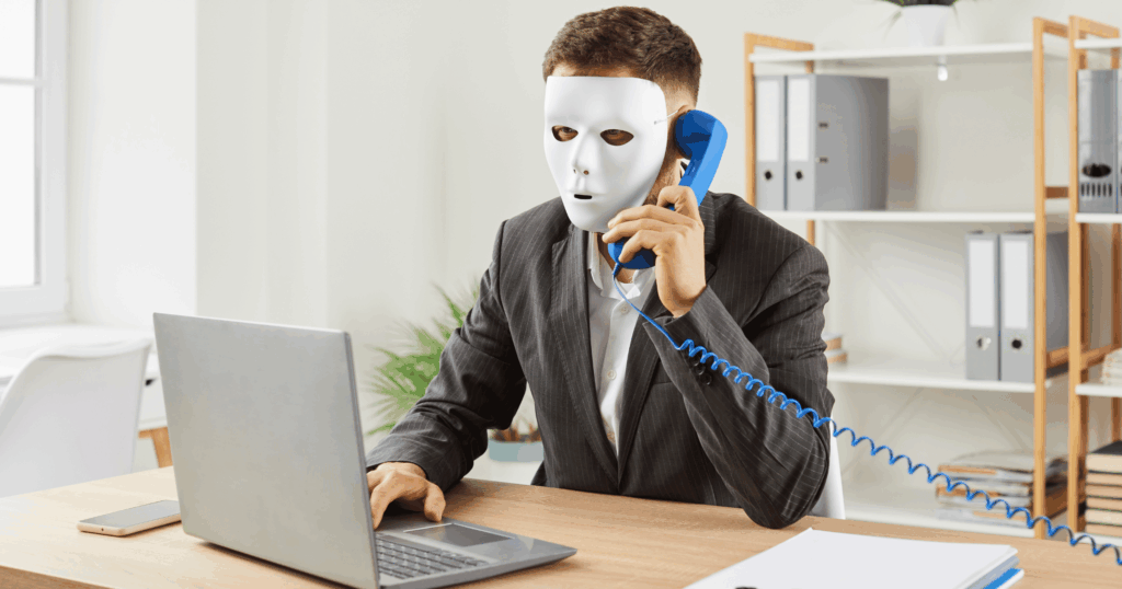 Masked scammer using a laptop and phone, representing online property fraud