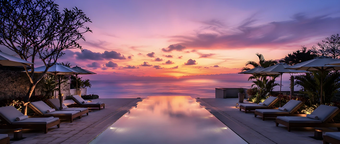 Infinity pool facing the ocean at sunset, with sun loungers and umbrellas on both sides